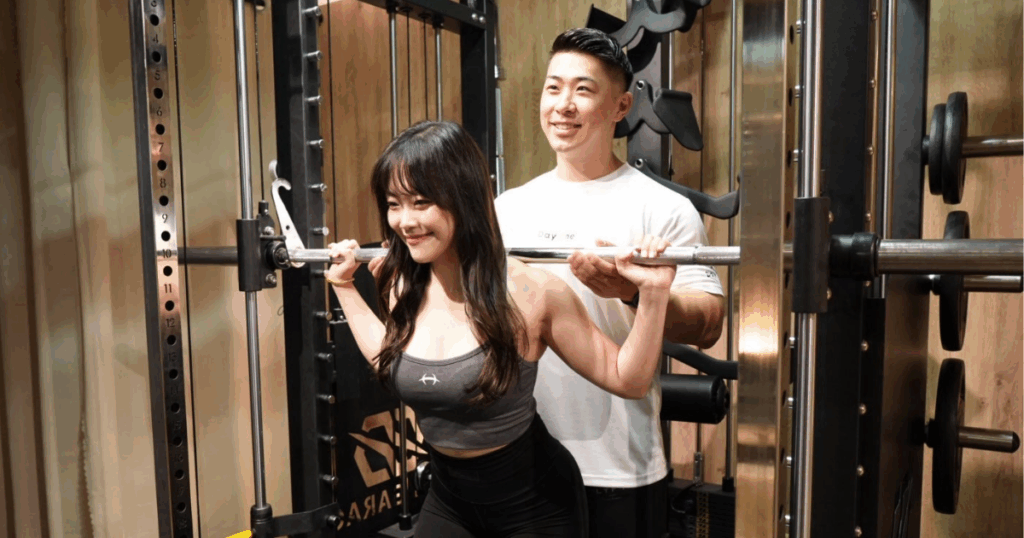 トレーナーが女性にスクワットを教えている写真